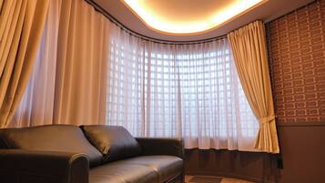 A modern room with a leather sofa, large windows with sheer curtains, and a patterned wall.