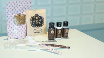 A bathroom vanity with a white countertop, a pink toothbrush holder, a Q-pot cafe branded bag, and four Q-pot cafe hair care products.