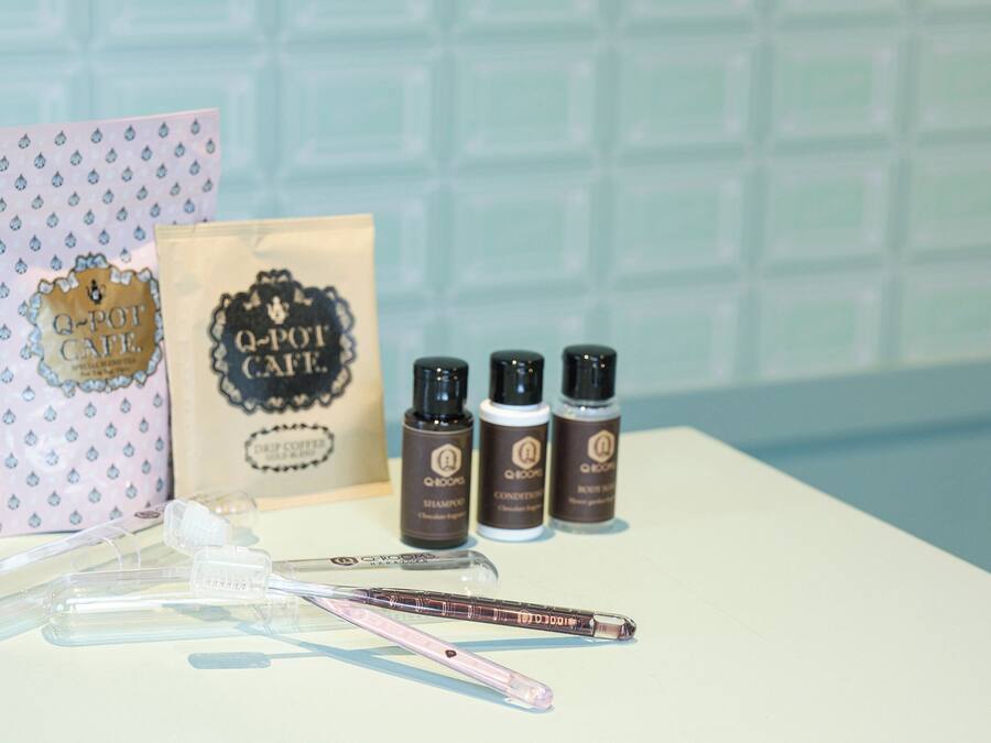 A bathroom vanity with a white countertop, a pink toothbrush holder, a Q-pot cafe branded bag, and four Q-pot cafe hair care products.