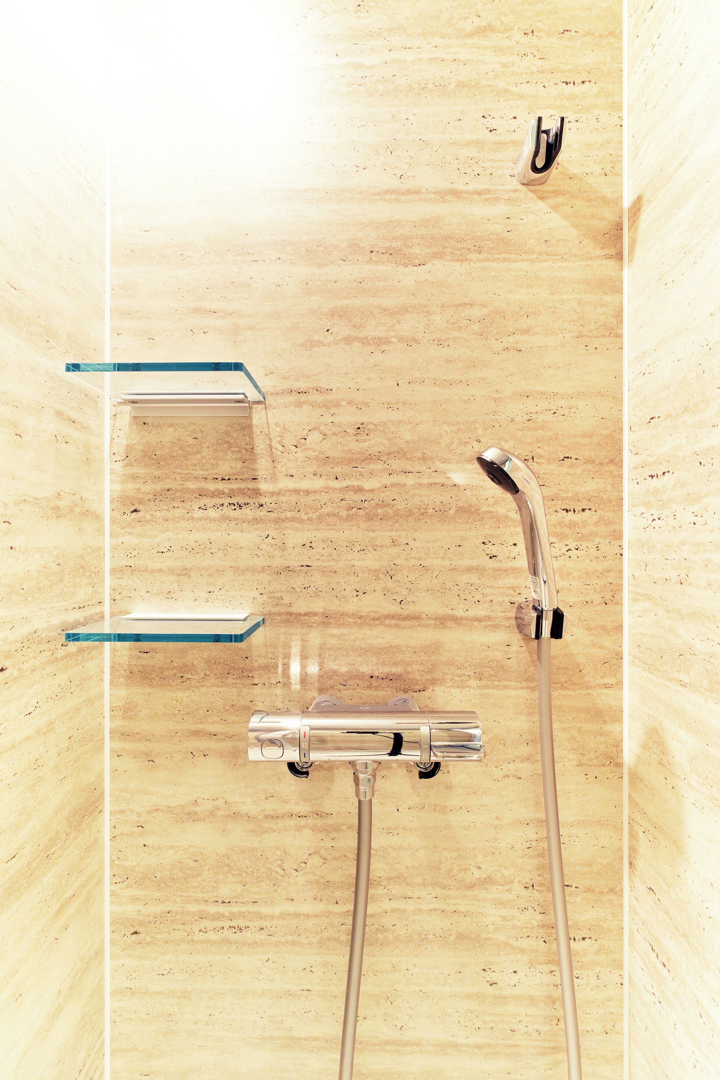 A bathroom with a wooden wall, a shower with a handheld showerhead, and two clear glass shelves.