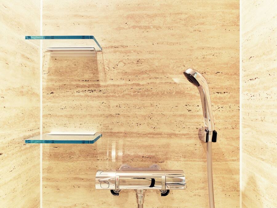 A bathroom with a wooden wall, a shower with a handheld showerhead, and two clear glass shelves.