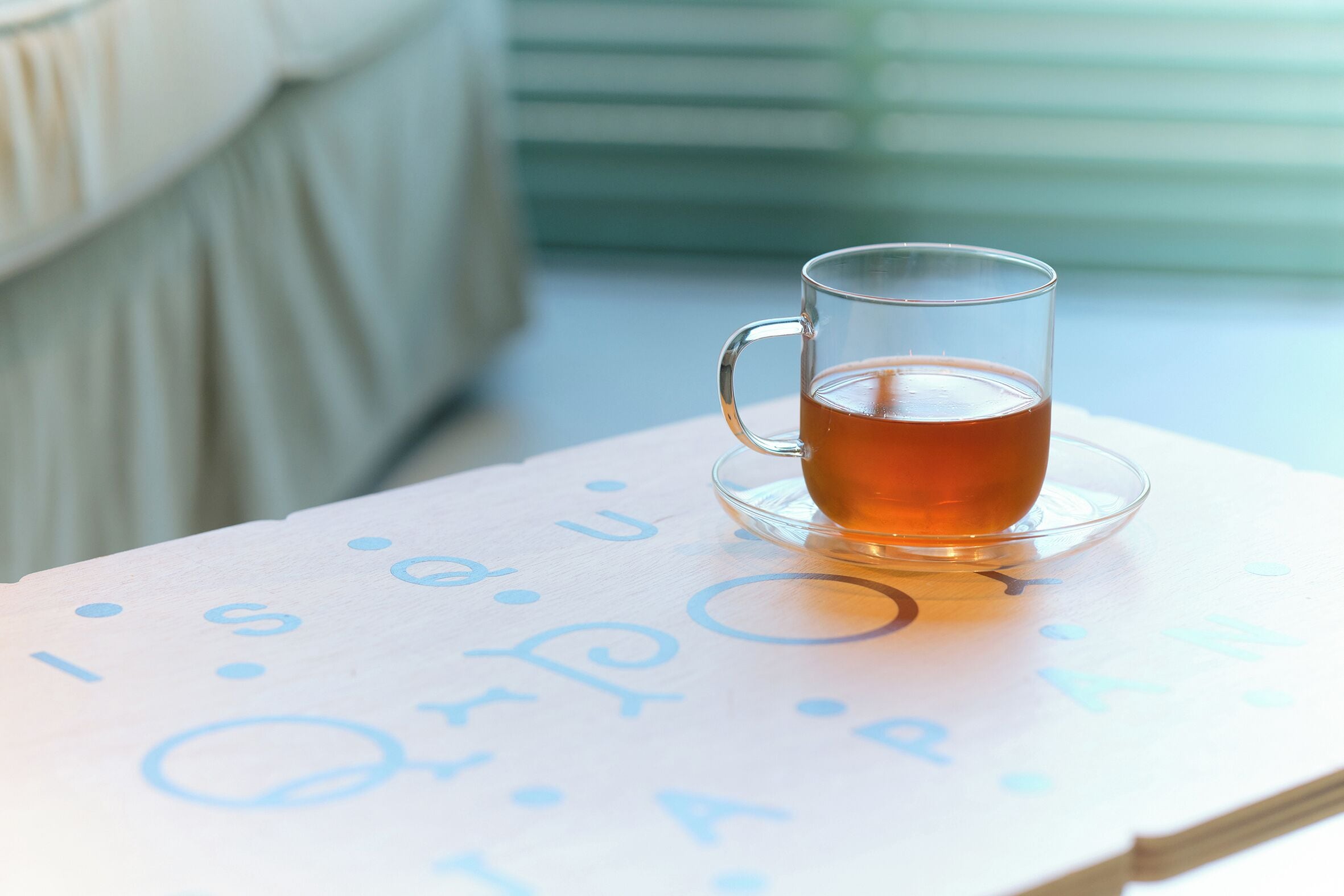 Una taza de té de vidrio transparente sobre un platito, apoyada sobre un libro con texto visible.