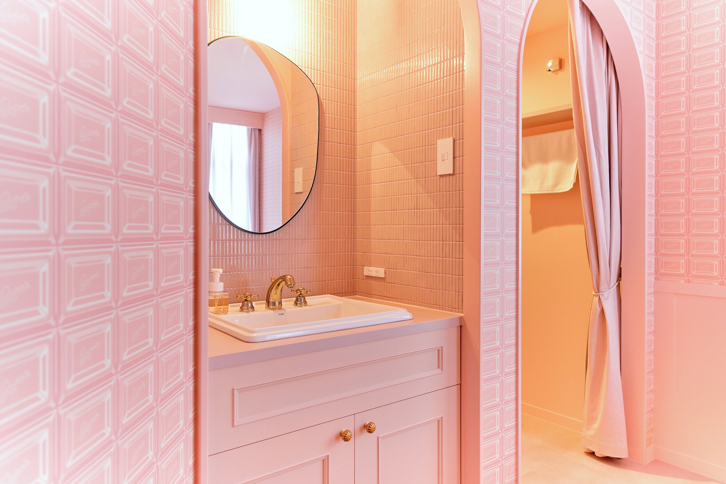 Un baño con un lavamanos blanco, un espejo redondo y una pared con azulejos rosas.