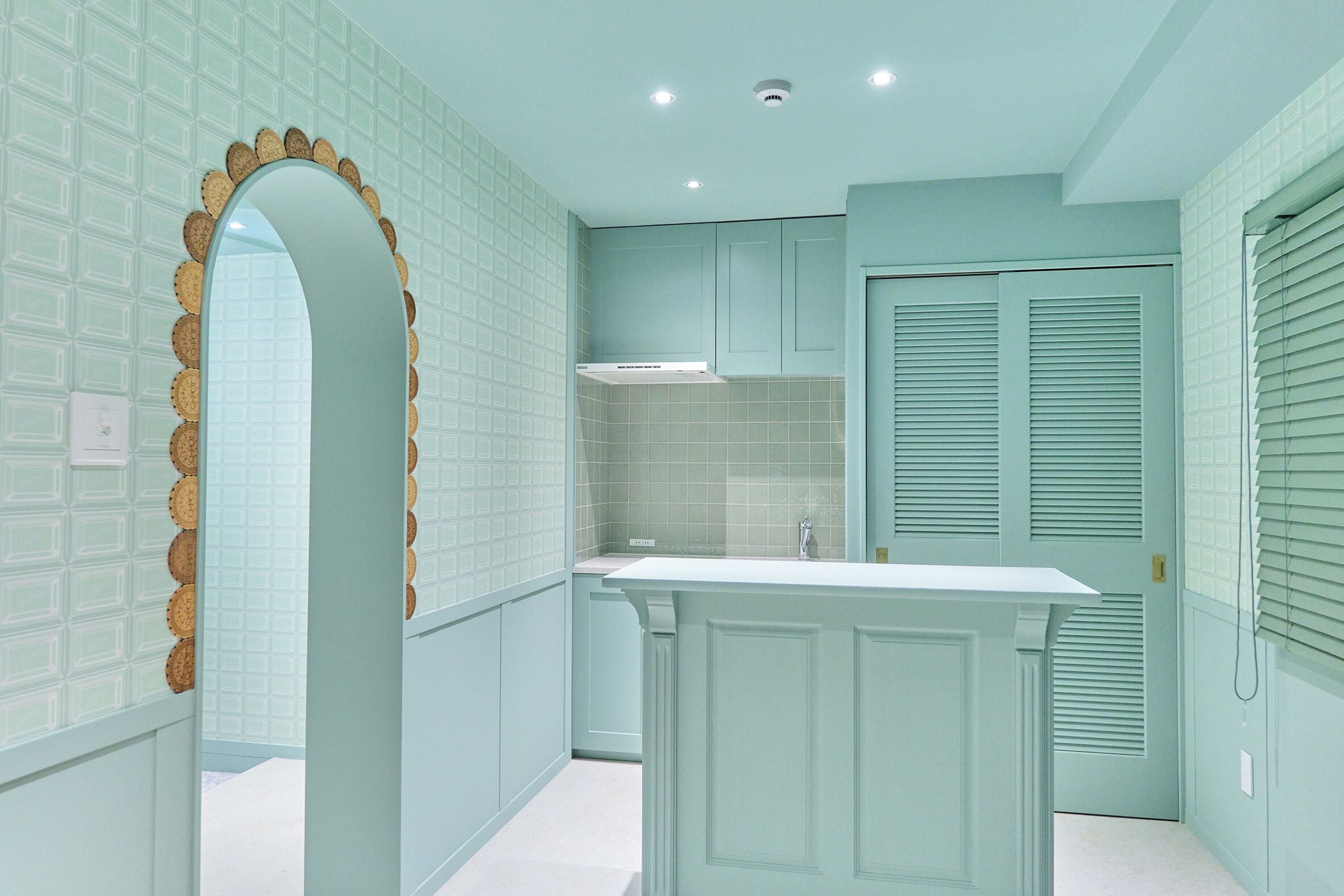A kitchen with light blue cabinetry, a white countertop, and a decorative archway.