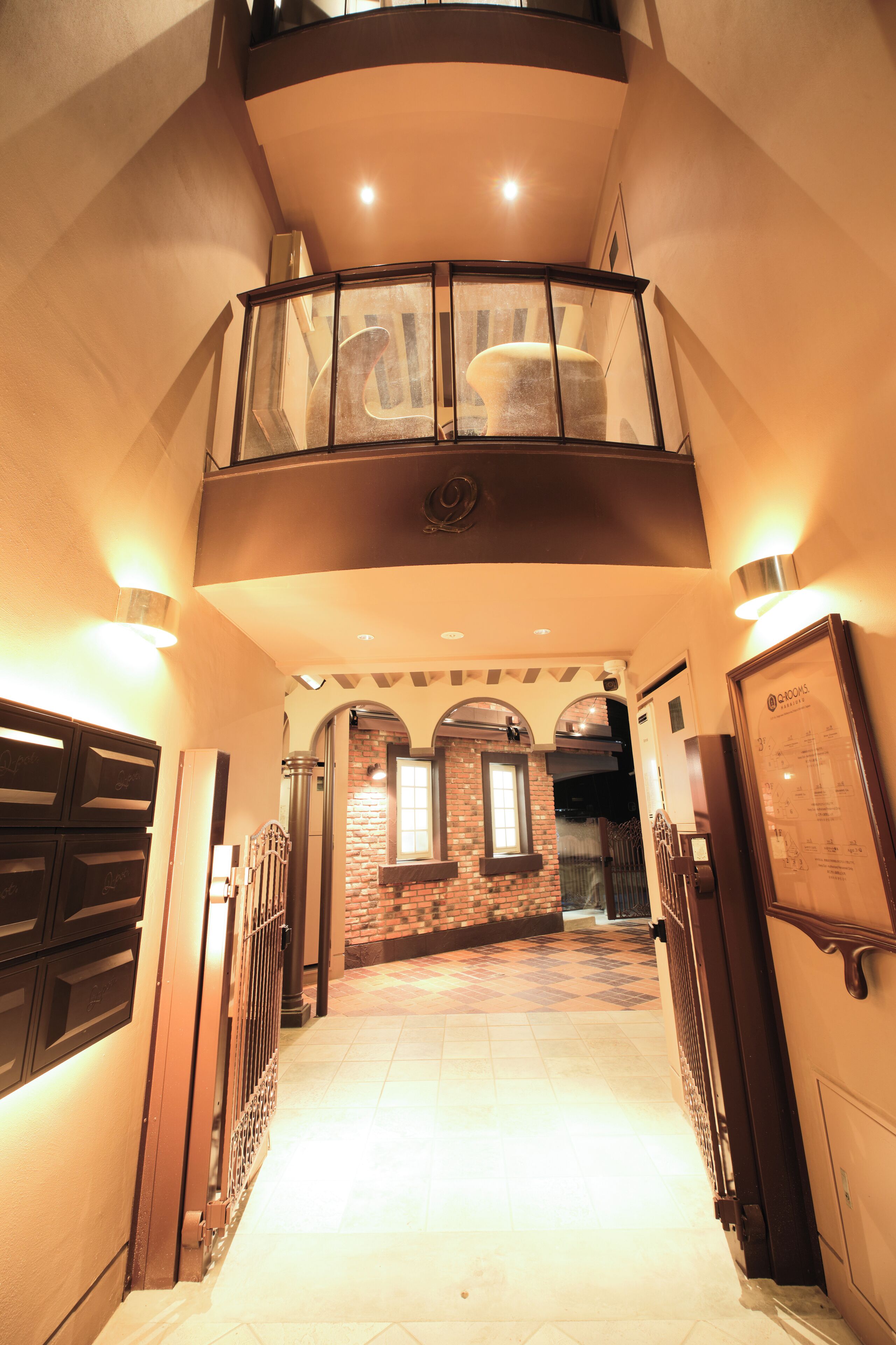 A spacious hallway with a high ceiling, a glass railing on the upper level, and a brick wall at the end.