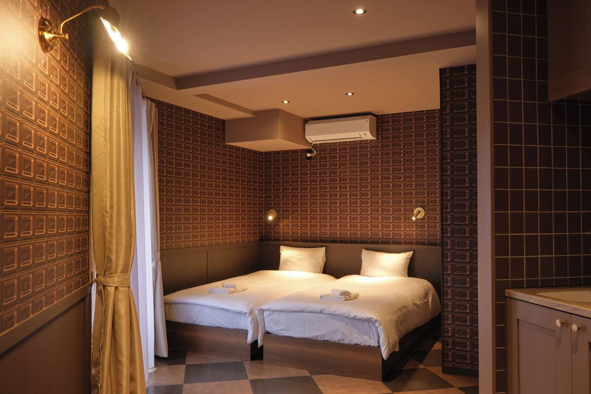 A hotel room with two beds, a shower, a sink, and an air conditioning unit.
