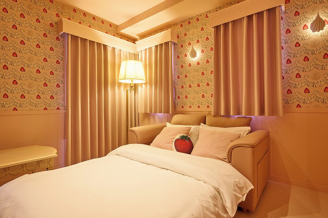 A hotel room with a bed, curtains, a lamp, and a wall with a pattern.