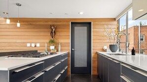 Une cuisine moderne dotée d’un îlot central, de murs recouverts de panneaux en bois et d’une porte noire au motif ajouré.