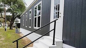 A residential building with a staircase leading to the entrance, a tree in the background, and a trash can near the steps.