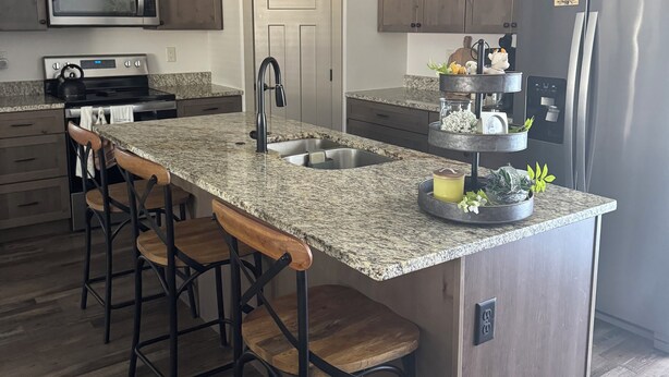 A modern kitchen with granite countertops, stainless steel appliances, and wooden bar stools. - Charming 3-bedroom townhome in Sturgis bordering the Black Hills (Sturgis)