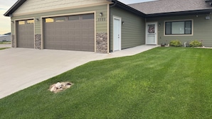 A two-story house with a garage, a stone accent wall, and a well-maintained lawn. - Charming 3-bedroom townhome in Sturgis bordering the Black Hills (Sturgis)