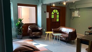 A spacious living room with a large window, leather sofas, a small round table, and a potted plant. - Glur Hostel Pattaya Walking Street (Pattaya)
