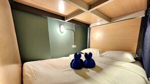 A bed with two plush toys, a wall-mounted light, and a wooden headboard. - Glur Hostel Pattaya Walking Street (Pattaya)