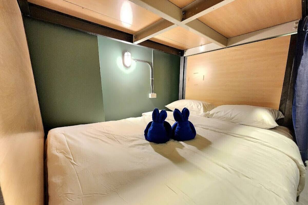 Ein Bett mit zwei Kuscheltieren, einer Wandleuchte und einem hölzernen Kopfteil.
