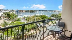 Een balkon met uitzicht op een jachthaven, een klein tafeltje en twee stoelen.