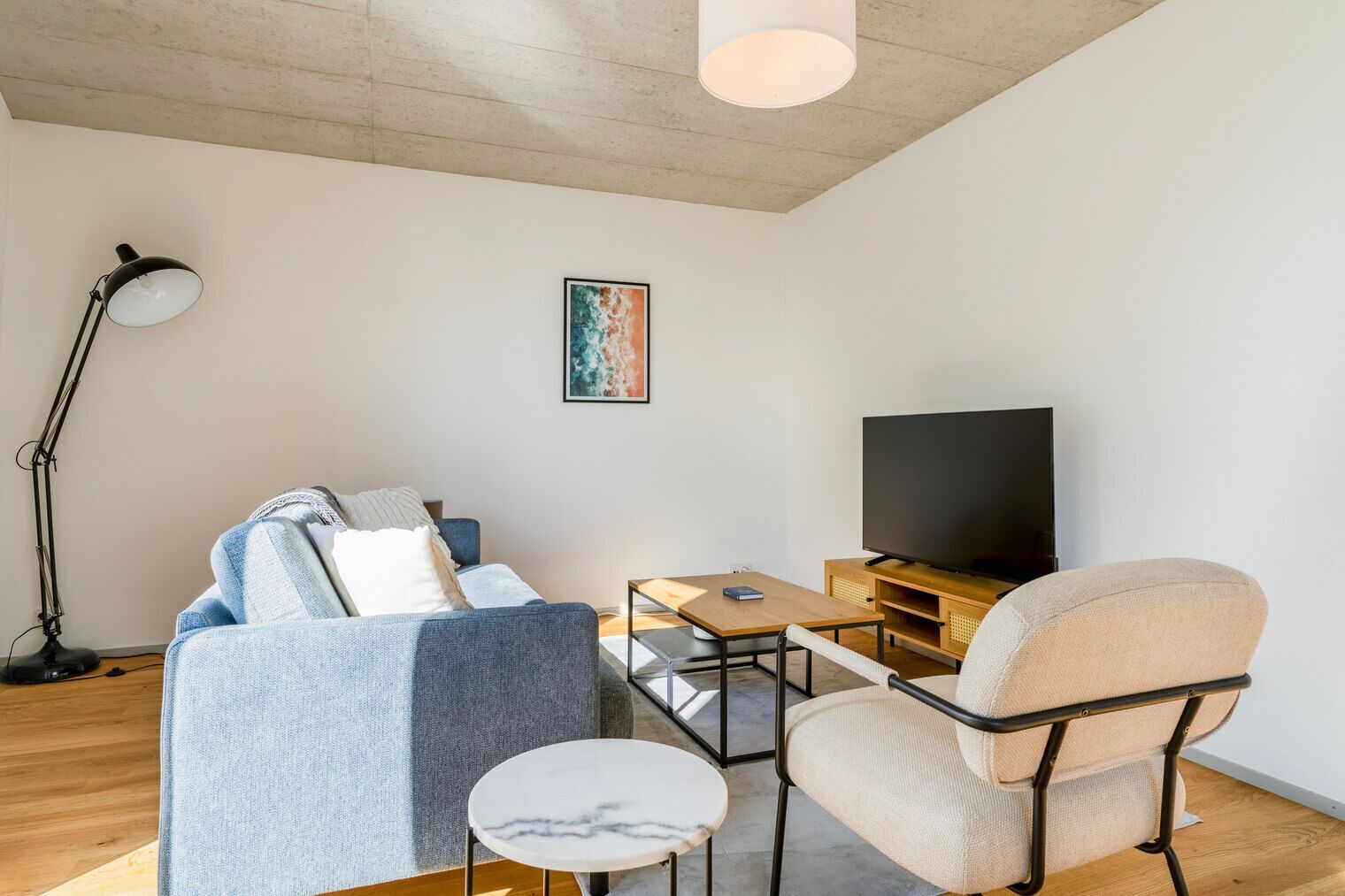 Una sala de estar moderna con un sofá, un sillón, una mesa de centro y un televisor de pantalla plana.