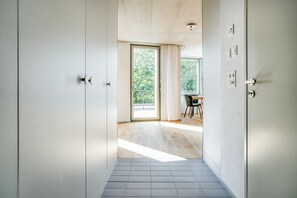 Un couloir menant à un balcon d’où l’on peut admirer les arbres, un coin repas avec des chaises et une porte dotée d’un interrupteur.
