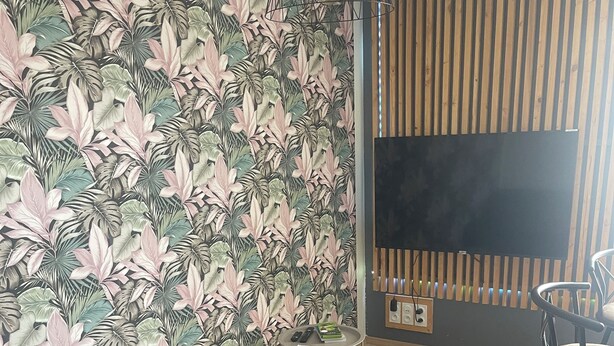 Un salon moderne avec un canapé gris, un mur lambrissé en bois et un grand téléviseur à écran plat.