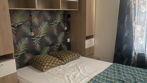 Une chambre à coucher avec un lit, une tête de lit ornée d’un motif de feuilles, un luminaire suspendu et une fenêtre avec des rideaux.