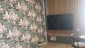 Un salon comprenant un canapé, un téléviseur fixé à un mur en bois, une petite table avec des télécommandes et un fauteuil.