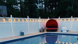 A swimming pool with a tiled deck, a basketball hoop, and a white fence with decorative lights. - Trackside Guesthouse w/ Pool (Clifton Park)