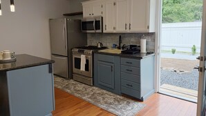 A compact kitchen with white cabinets, a stainless steel refrigerator, a microwave, a stove, and a sink. - Trackside Guesthouse w/ Pool (Clifton Park)