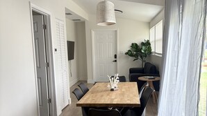 A dining area with a wooden table and black chairs, a hanging light fixture, and a view of a garden through sheer curtains. - Paloma Hideaway (St. Petersburg)