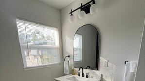 A bathroom with a white vanity, a large mirror, and a window with blinds. - Paloma Hideaway (St. Petersburg)