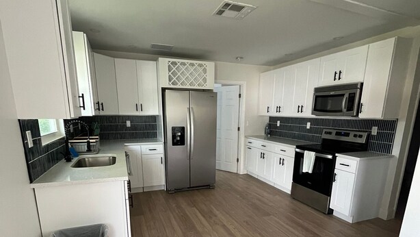 A modern kitchen with white cabinets, a stainless steel refrigerator, a microwave, and a black trash bin. - Paloma Hideaway (St. Petersburg)