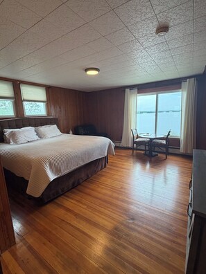 A room with a large bed, a wooden floor, a ceiling fan, and a view of the water. - Enjoy Breath-taking Lake and Mountains views at the Belknap Point inn House (Gilford)
