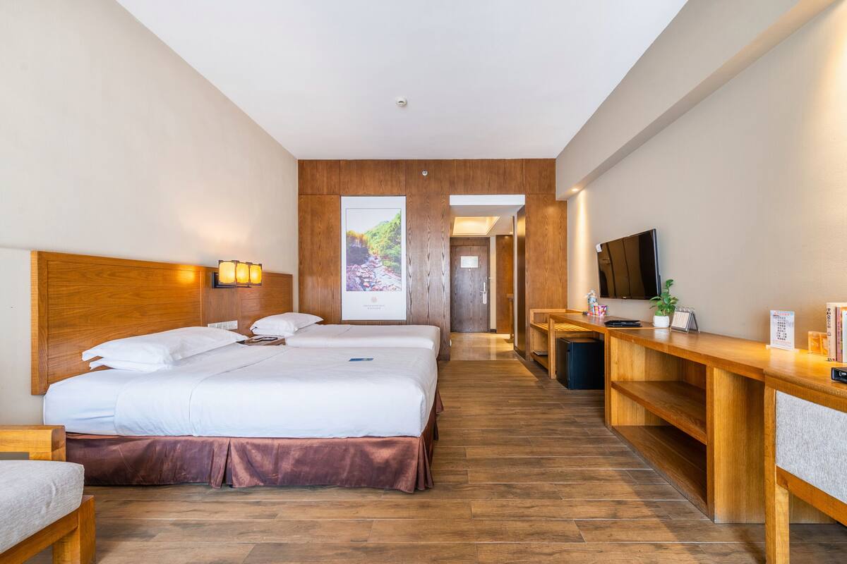 A hotel room with a large bed, a desk, a TV, and a view of a mountainous landscape.