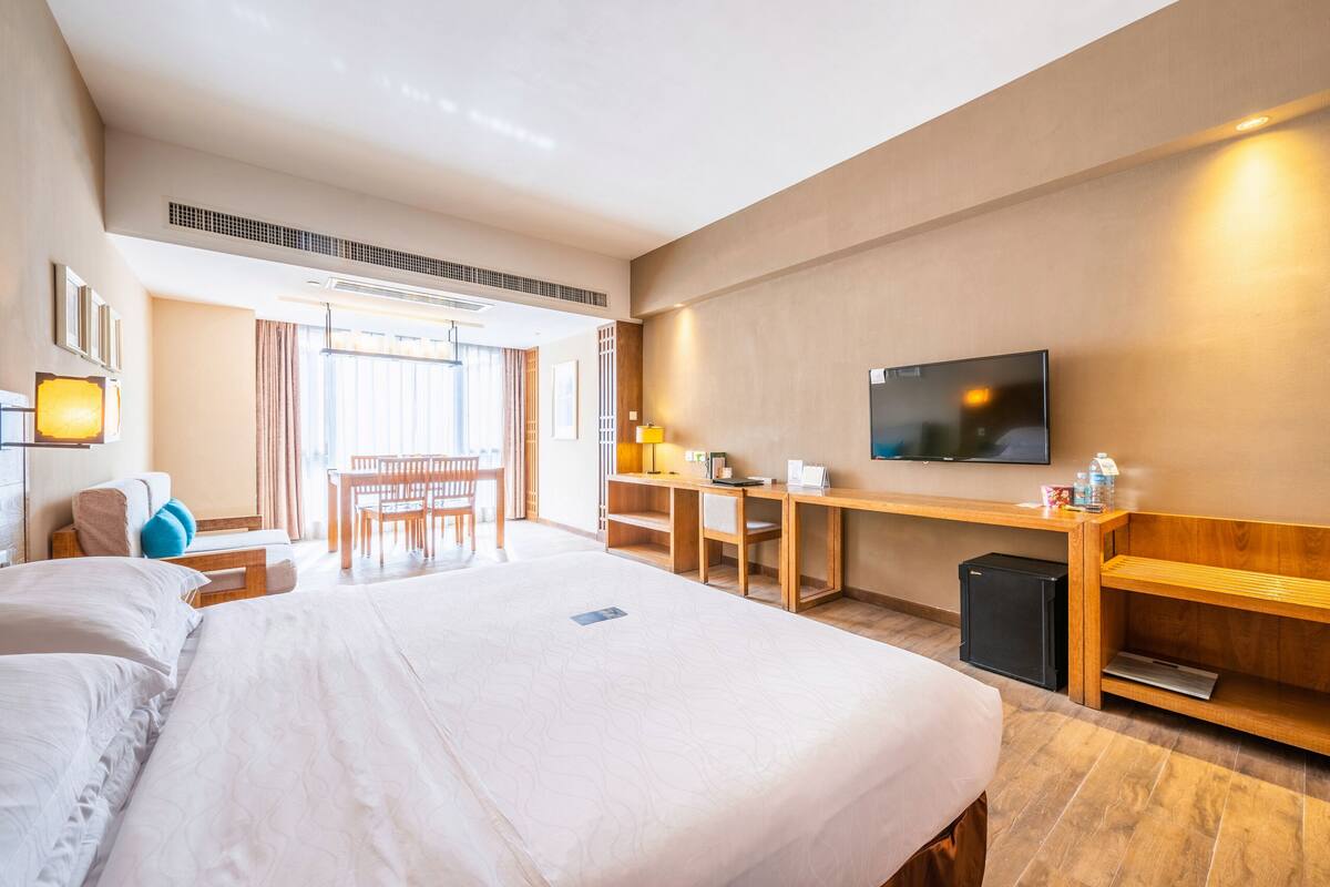 A hotel room with a large bed, a desk, a chair, a TV, and a small fridge.