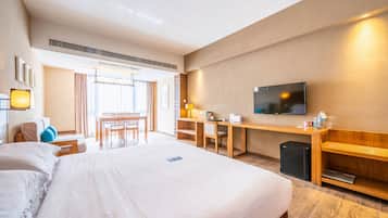 A hotel room with a large bed, a desk, a chair, a TV, and a small fridge.