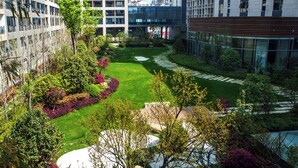 A modern urban courtyard with a well-maintained lawn, pathways, and surrounding greenery.