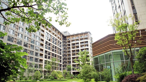A modern residential building complex with multiple floors, a central courtyard with a curved pathway, and surrounding greenery.