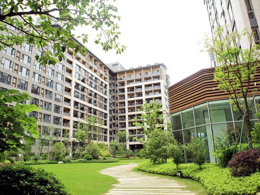 A modern residential building complex with multiple floors, a central courtyard with a curved pathway, and surrounding greenery.