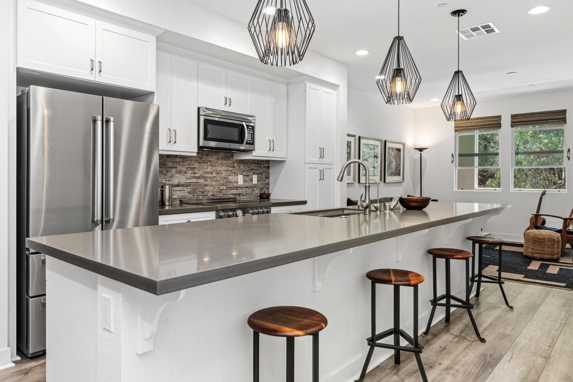 A modern kitchen with stainless steel appliances, a large island with stools, and pendant lighting.