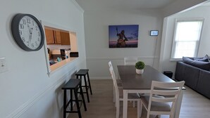Ein Essbereich mit einem Holztisch, weißen Stühlen und einer Uhr an der Wand.