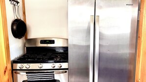 Una cocina compacta con estufa y refrigerador de acero inoxidable, vigas de madera en el techo y piso de madera.
