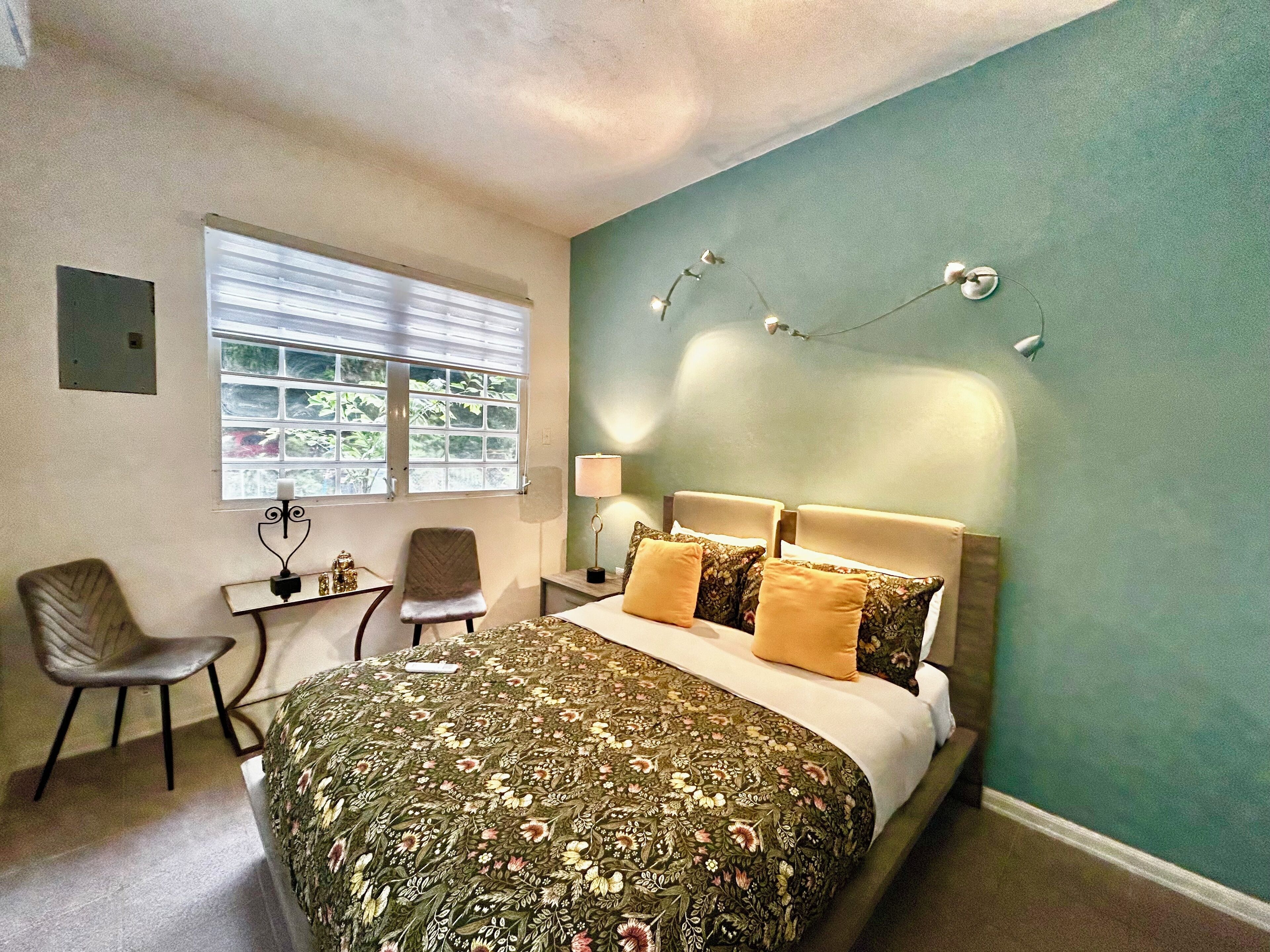 A hotel room with a bed, two chairs, a small table, a lamp, and a window with blinds.