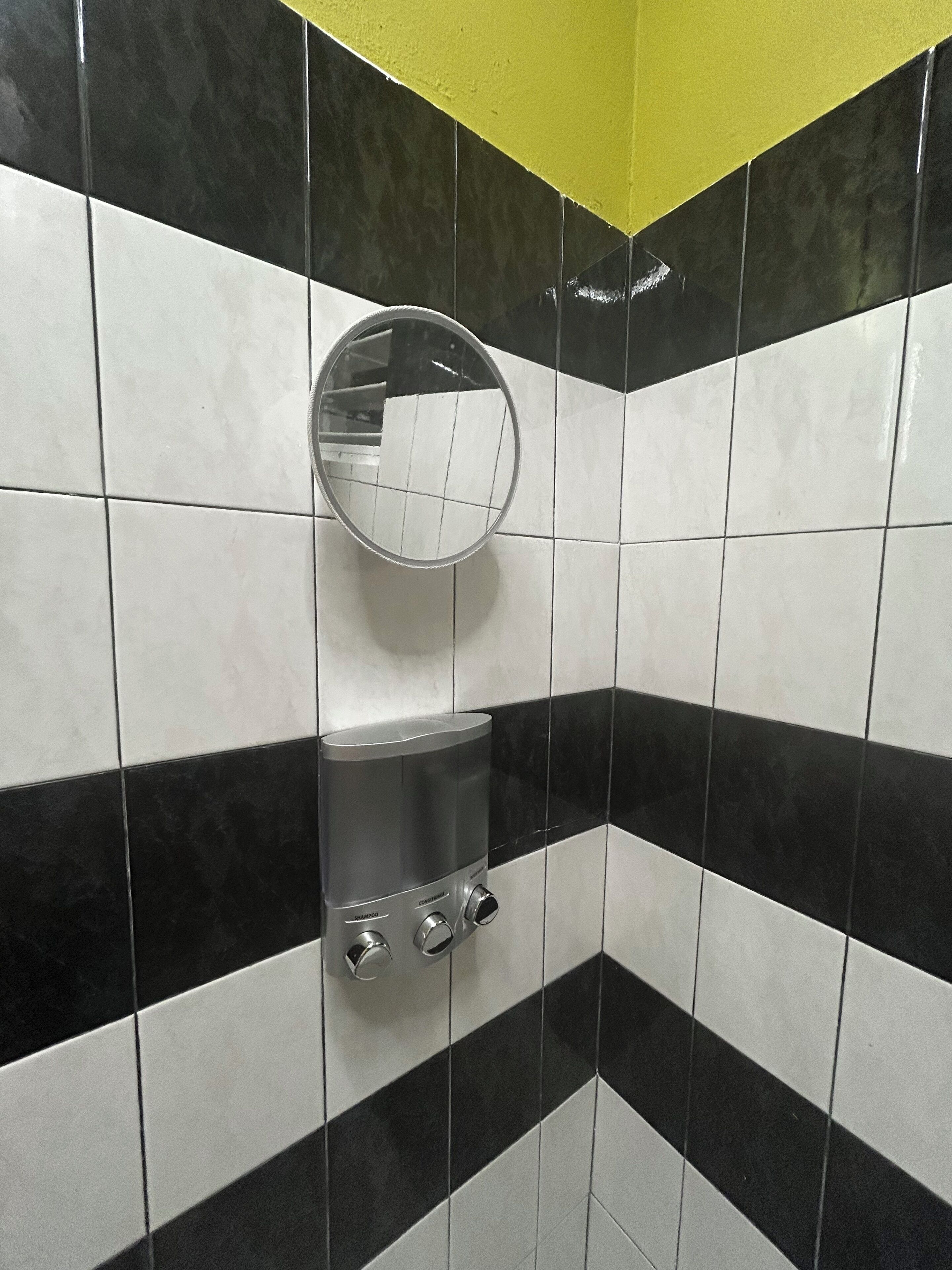 Une salle de bain avec des carreaux noirs et blancs, un miroir et un distributeur de savon.