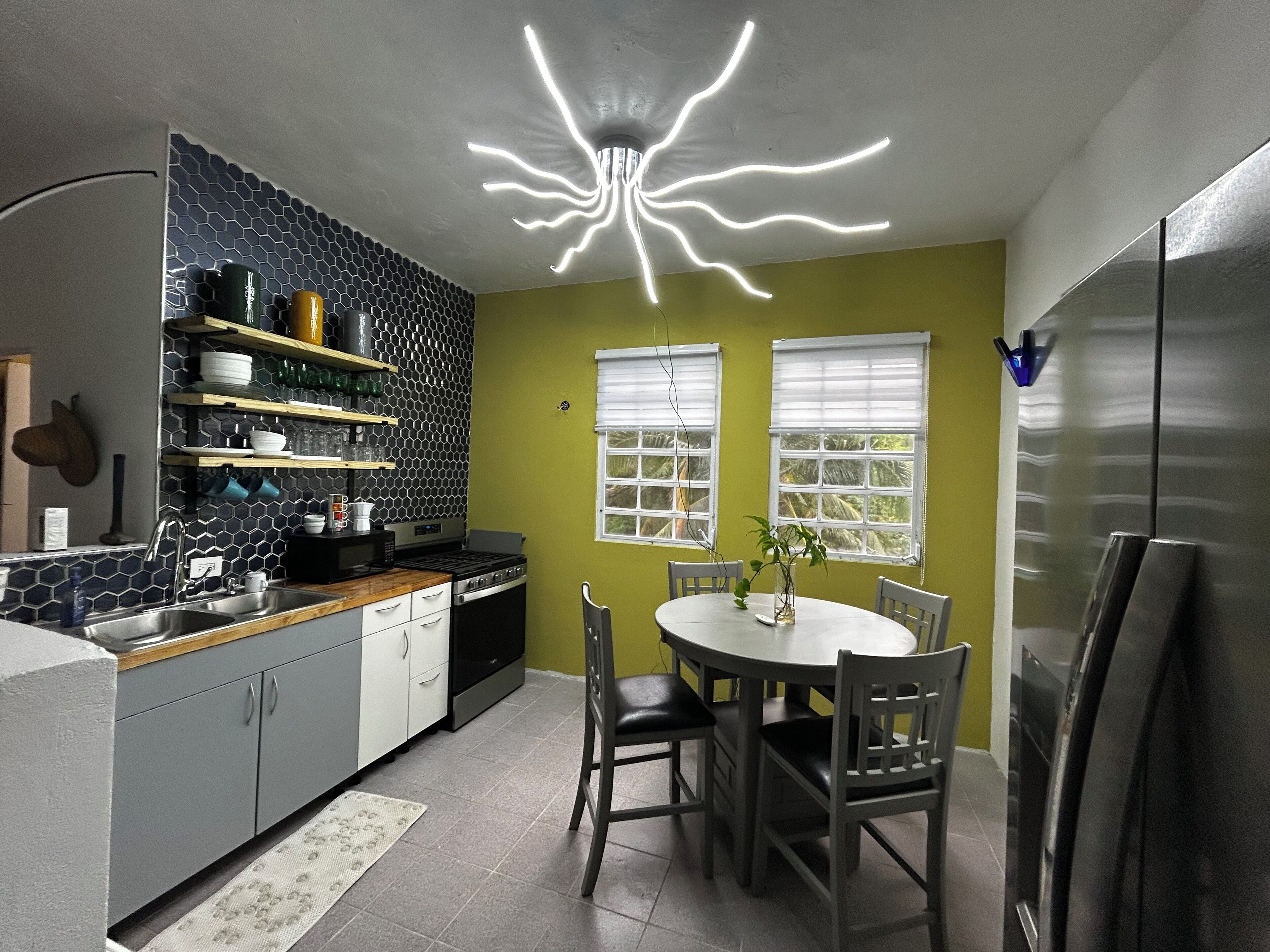 A modern kitchen with a central island, a dining table with chairs, and a unique ceiling light fixture.