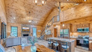 A spacious log cabin interior with a large dining area, kitchen, and a staircase leading to an upper level. - Tranquil cabin with in charming Mineral Bluff with beautiful views (Mineral Bluff)