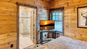 A wooden cabin interior with a glass shower, a bed with patterned bedding, a television on a stand, and a framed deer antler on the wall. - Tranquil cabin with in charming Mineral Bluff with beautiful views (Mineral Bluff)