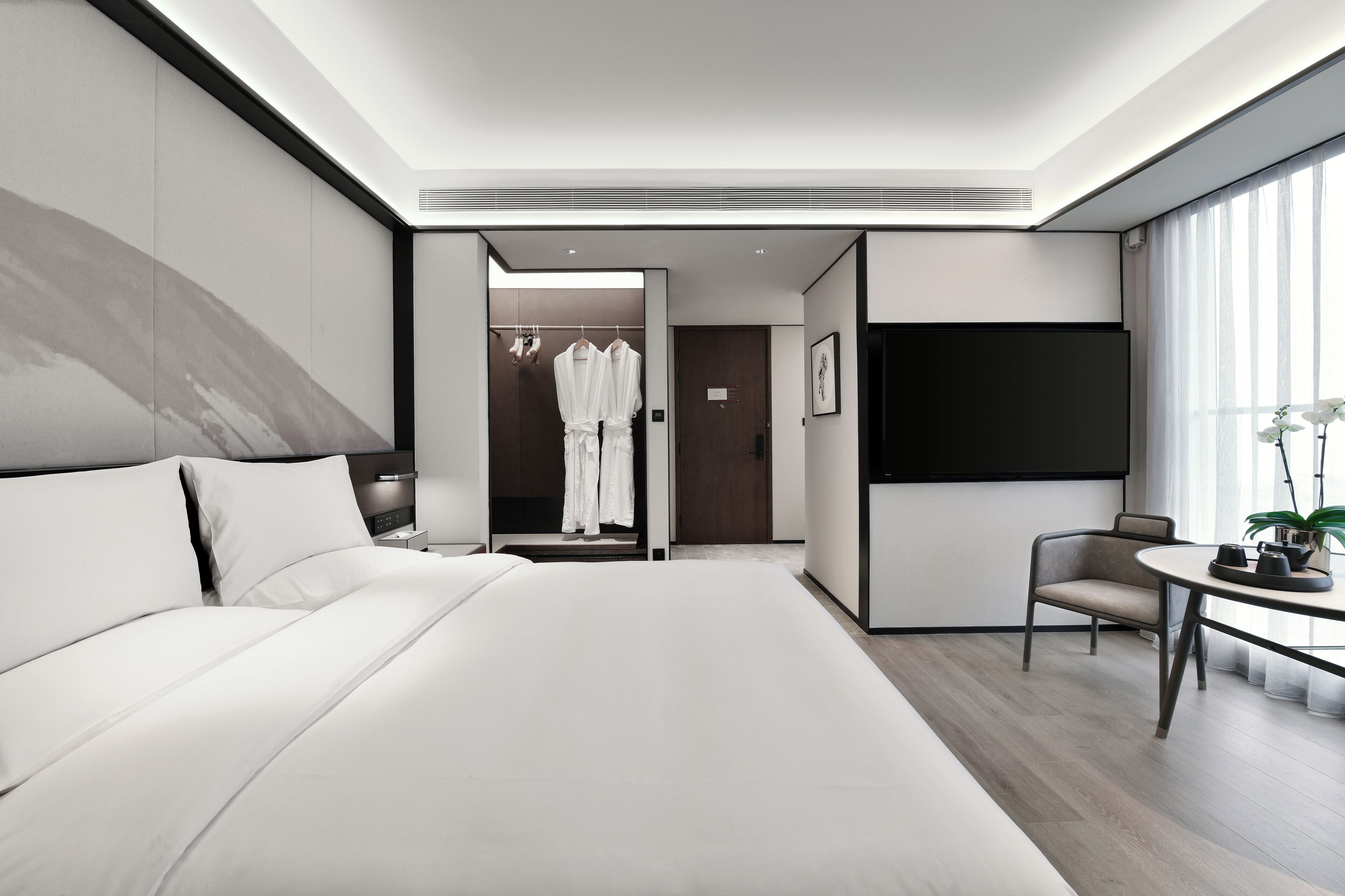 A modern hotel room with a large bed, a seating area, a TV, and a walk-in closet.