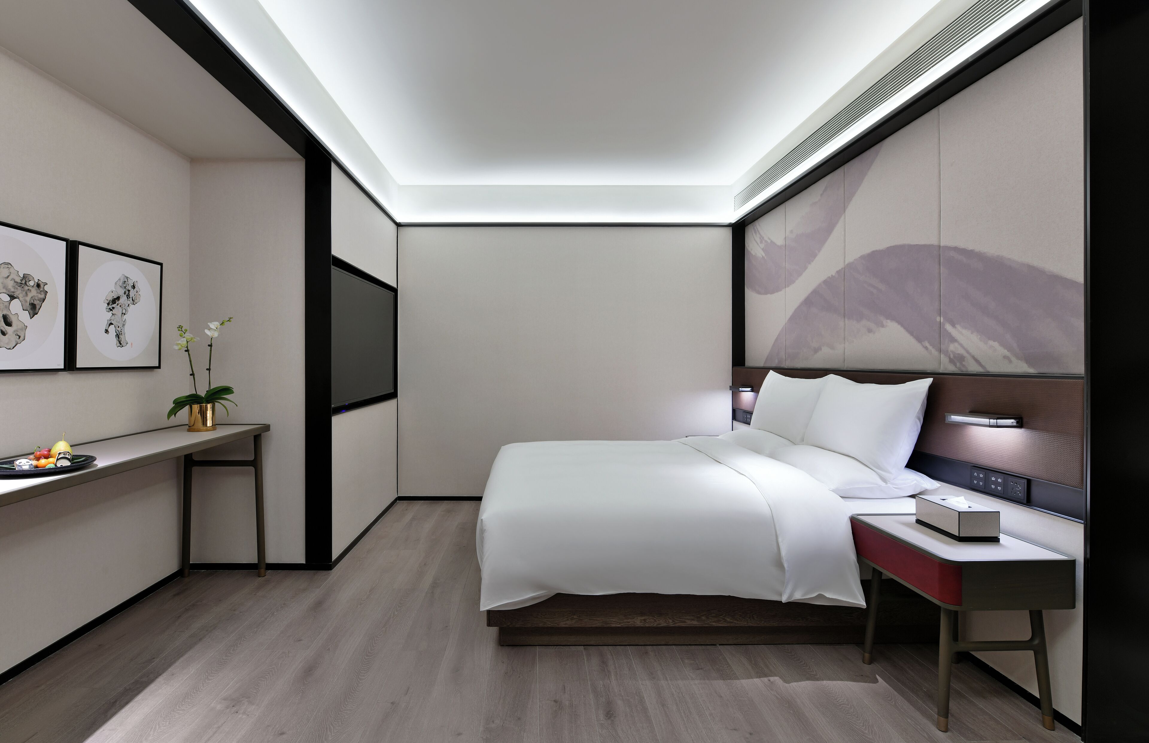 Une chambre d’hôtel moderne, équipée d’un lit, d’une table de chevet, d’un bureau et ornée d’œuvres d’art sur les murs.