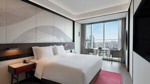 A modern hotel room with a large bed, a bedside table, a desk, and a view of the city through large windows. - JOYA Hotel Chengdu Taikoo Li IFS (Chengdu)