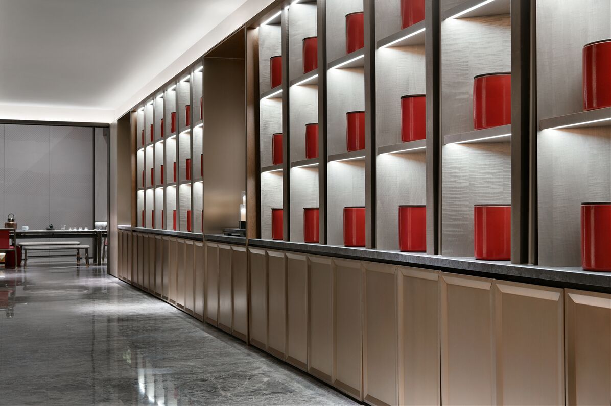 A modern hotel corridor with a long reception desk, a seating area, and a wall with illuminated red cylindrical objects.
