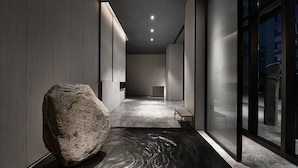 A modern hallway with a large rock, a bench, and a glass wall. - JOYA Hotel Chengdu Taikoo Li IFS (Chengdu)