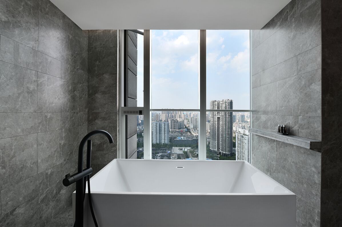 Ein modernes Badezimmer mit einer großen Badewanne, einem schwarzen Wasserhahn und Blick auf eine Stadtlandschaft durch ein großes Fenster.